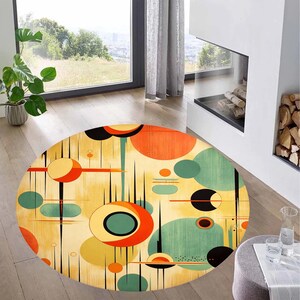 May include: An oval rug with a mid-century modern design. The rug has a cream background with orange, green, black, and yellow geometric shapes. The rug is placed on a wooden floor in a living room setting.