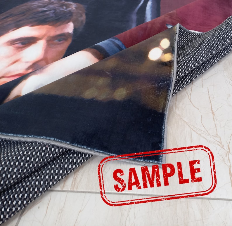 May include: Close-up of a rug with a black and white patterned backing. The rug has a printed image of a man's face and a blurred background. The rug is labeled "SAMPLE".