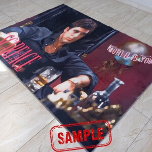 May include: A red and black rug with a picture of a man in a black shirt and a gold chain. The text "Scarface" is in pink letters and the text "World is yours" is in white letters.