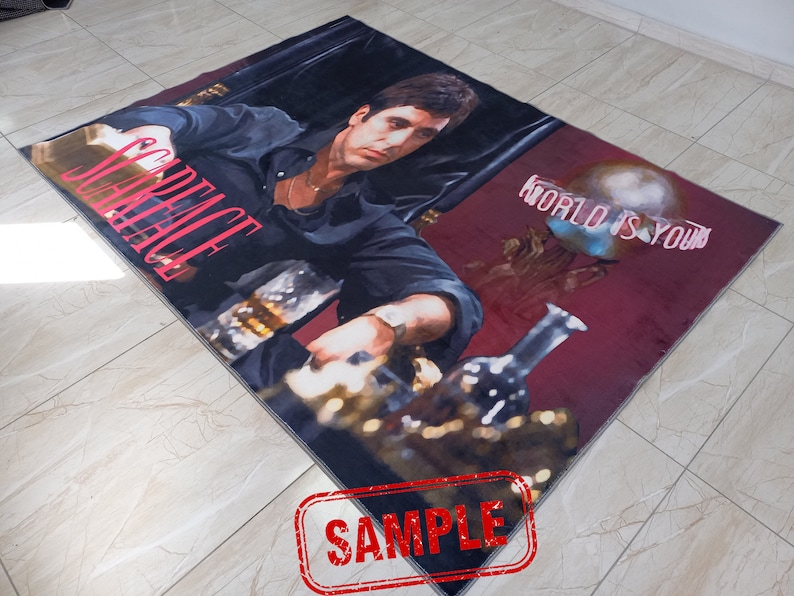 May include: A red and black rug with a picture of a man in a black shirt and a gold chain. The text "Scarface" is in pink letters and the text "World is yours" is in white letters.
