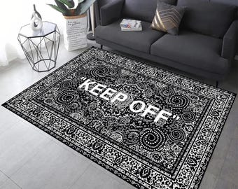 May include: Black and white patterned area rug with the text "KEEP OFF" in white. The rug features a detailed paisley-like design and a decorative border. The rug is rectangular and placed on a tiled floor.