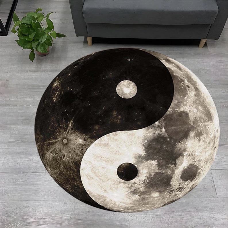 Może przedstawiać: Okrągły dywan z wzorem yin yang. Symbol yin yang składa się z dw&oacute;ch poł&oacute;wek, jednej czarnej i jednej białej, z małym k&oacute;łkiem przeciwnego koloru w każdej połowie. Dywan jest wykonany tak, aby przypominał powierzchnię księżyca.
