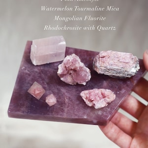 Könnte beinhalten: Eine Sammlung von rosa Kristallen auf einer violetten Platte. Die Kristalle umfassen eine Platte aus Lavendel-Rosenquarz, rosa Islandspat, rosa Amethyst, Wassermelonen-Turmalin-Glimmer, mongolische Fluorit und Rhodochrosit mit Quarz.