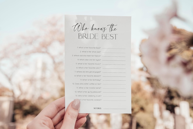 Puede incluir: Una tarjeta blanca con el texto "Who knows the BRIDE BEST" en escritura elegante. La tarjeta presenta una serie de preguntas para completar sobre la novia, perfectas para un juego de despedida de soltera. La tarjeta es sostenida por una persona.