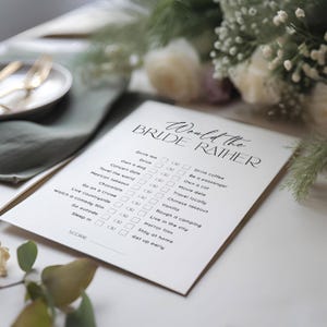 May include: A white card with the text "Would the Bride Rather" in black script. The card features a list of 16 questions with two choices each, such as "Drink tea or Drink coffee" and "Own a dog or Own a cat".  Each choice has a checkbox next to it.