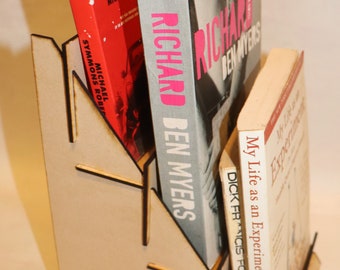 Puede incluir: Un soporte de libros de madera con tres estantes sostiene tres libros. El libro superior es rojo con el título "Patrick's Alphabet". El libro del medio es blanco con el título "Richard Ben Myers". El libro inferior es blanco con el título "My Life as an Experiment, A.J. Jacobs".