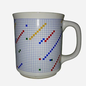 May include: A white ceramic mug featuring a blue grid pattern across the exterior surface. The grid is accented with scattered diagonal lines and individual squares in primary colours including red, yellow, blue, and green, with a curved handle.
