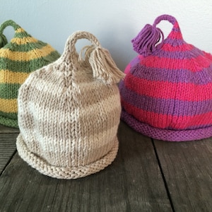 May include: Three striped knitted hats with tassels. The hats are green and yellow, beige and white, and pink and purple.