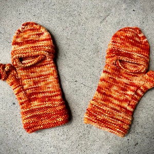 Könnte beinhalten: Ein Paar gestrickte Fingerhandschuhe in orange und weißen Streifen mit einem umgeschlagenen Bündchen. Die Handschuhe haben einen Daumenloch und ein fingerloses Design.