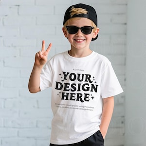 Könnte beinhalten: Ein weißes T-Shirt mit dem Text "YOUR DESIGN HERE" in fetten schwarzen Buchstaben, getragen von einer Person mit schwarzer Kappe und Sonnenbrille. Das Shirt enthält auch den Text "K.C STUDIO" und eine Textzeile darunter mit der Aufschrift "Create your visual/graphic using Photoshop, Canva, or other preferred editing software."