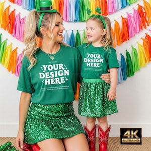 Puede incluir: Dos personas con camisetas verdes a juego con el texto "YOUR DESIGN HERE" en blanco y faldas con lentejuelas. Una lleva un sombrero verde, la otra una diadema con tréboles. Botas de vaquero rojas completan el conjunto.