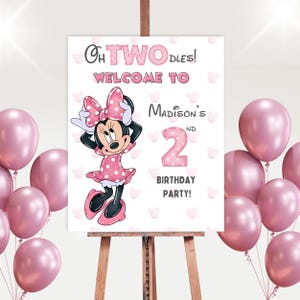 May include: A party sign on an easel with the text "Oh TWO-dles! Welcome to Madison's 2nd Birthday Party!" features a Minnie Mouse illustration and pink balloons. The sign is white with pink polka dots and hearts.
