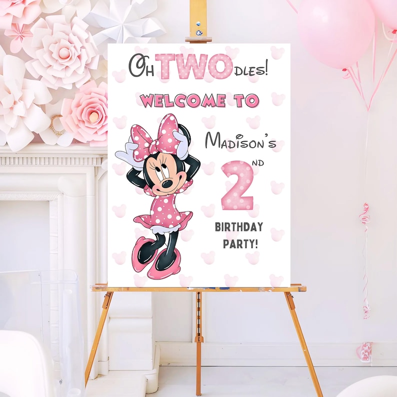 May include: A wooden easel displays a party sign with Minnie Mouse. The sign reads "Oh Two-dles! Welcome to Madison's 2nd Birthday Party!" Minnie Mouse is in a pink polka dot dress and bow. Pink hearts and balloons decorate the background.