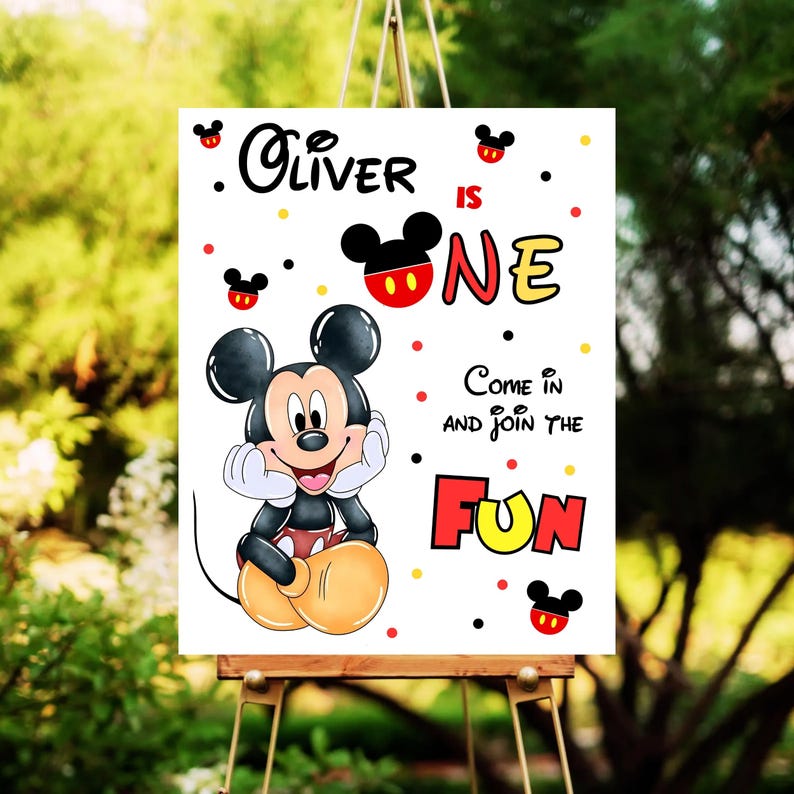 May include: A white sign featuring Mickey Mouse with the text "Oliver is ONE". The sign has a cartoon illustration of Mickey Mouse, red, yellow, and black accents, and the words "Come in and join the FUN".