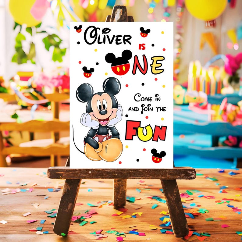 May include: A white sign on a wooden easel featuring Mickey Mouse and the text "Oliver is One." The sign includes the phrase "Come in and join the FUN" in red and yellow. The background is a party scene with balloons and confetti.