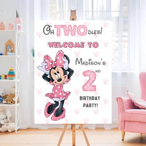 May include: A white sign on a wooden easel with the text "Oh TWO-dles! Welcome to Madison's 2nd Birthday Party!" Minnie Mouse is featured in a pink polka dot dress and bow.