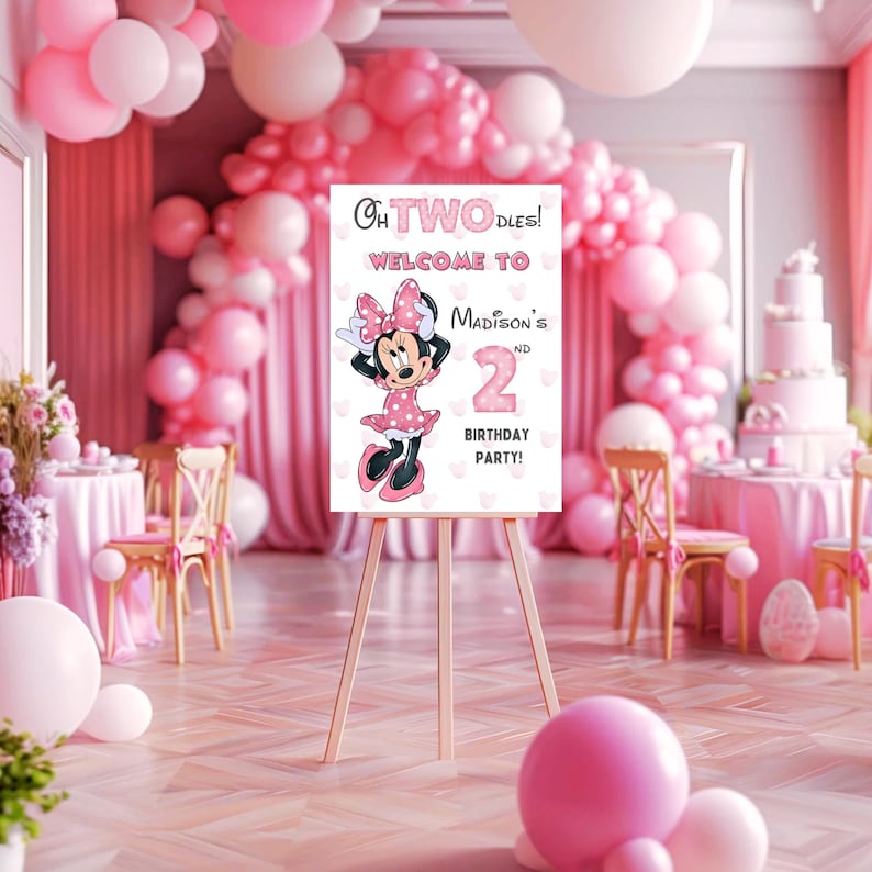 May include: A pink and white sign on a wooden easel with the text "Oh TWO-dles! Welcome to Madison's 2nd Birthday Party!" features a cartoon Minnie Mouse. The party decor includes pink balloons and a cake.
