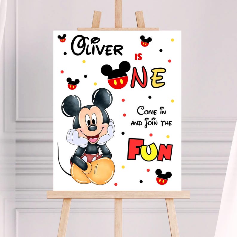 May include: A white sign on an easel featuring Mickey Mouse. The sign reads "Oliver is One" with the words "Come in and Join the Fun." Mickey Mouse is in the center, surrounded by red, yellow, and black accents.