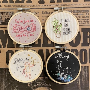 May include: Four embroidered hoops with different Harry Potter quotes. The first hoop is pink with the quote "You're just as sane as I am" and a graphic of Harry Potter's glasses. The second hoop is white with a cactus and the quote "I'm worth ten of you Malfoy!" The third hoop is white with the quote "Dobby is free" and a graphic of Dobby. The fourth hoop is black with the quote "Always" and a graphic of a stag.