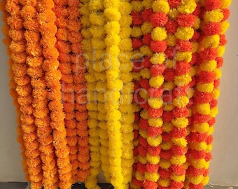 May include: A collection of marigold garlands in vibrant colors. The garlands are in shades of orange, yellow, and a mix of red and yellow. Each garland is made of densely packed, round marigold flowers, creating a full and textured appearance. The garlands are hanging vertically.
