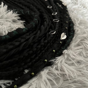 May include: Black and green synthetic dreadlocks with silver rings and a leaf charm.