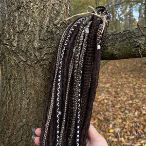 May include: A set of brown, grey, and white synthetic dreadlocks with silver beads. The dreadlocks are tied together with twine.