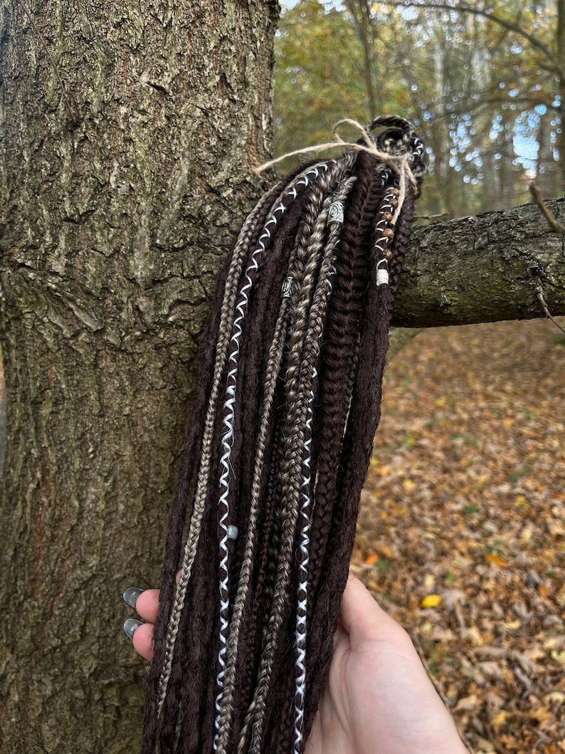 May include: A set of brown, grey, and white synthetic dreadlocks with silver beads. The dreadlocks are tied together with twine.