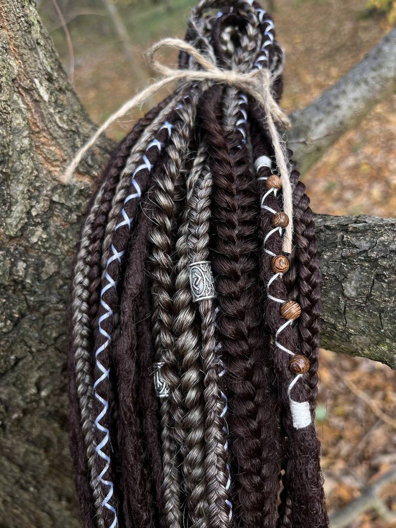 May include: A set of brown and grey synthetic dreadlocks with blue and white ribbon accents. The dreadlocks are tied together with twine and have wooden beads and metal beads.
