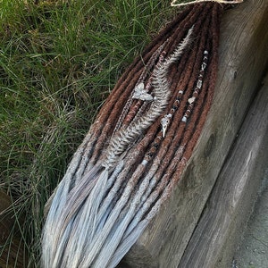 May include: A set of brown and white synthetic dreadlocks with beads and charms. The dreadlocks are tied together with a brown string.