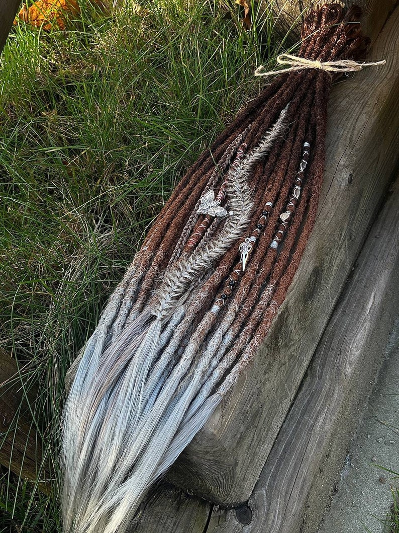 May include: A set of brown and white synthetic dreadlocks with beads and charms. The dreadlocks are tied together with a brown string.
