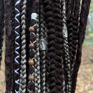 May include: A set of brown and grey dreadlocks with wooden beads and silver metal rings with runes. The dreadlocks are braided and have a variety of textures.