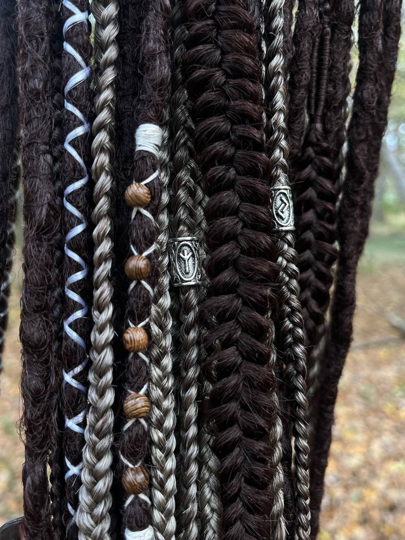 May include: A set of brown and grey dreadlocks with wooden beads and silver metal rings with runes. The dreadlocks are braided and have a variety of textures.