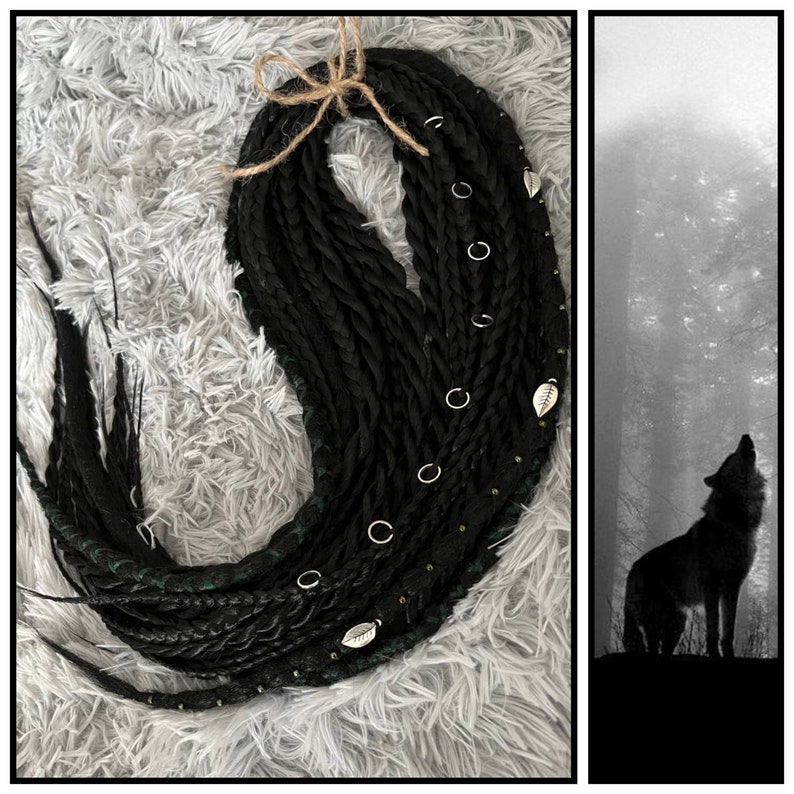 May include: Black and green synthetic dreadlocks with silver rings and leaf charms. The dreadlocks are arranged in a circle on a white fuzzy surface. A silhouette of a wolf howling at the moon is in the background.