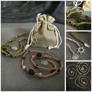 May include: Three handmade macrame cord necklaces with wooden beads and metal charms. The necklaces are displayed on a gray surface with a burlap bag in the background. The charms include a sun, a leaf, and a flower.