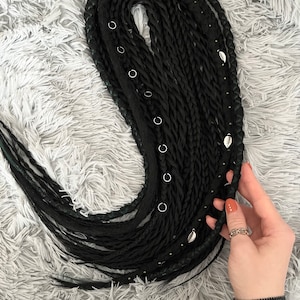 May include: A set of black synthetic hair extensions with silver beads and charms. The extensions are braided and have a textured look.