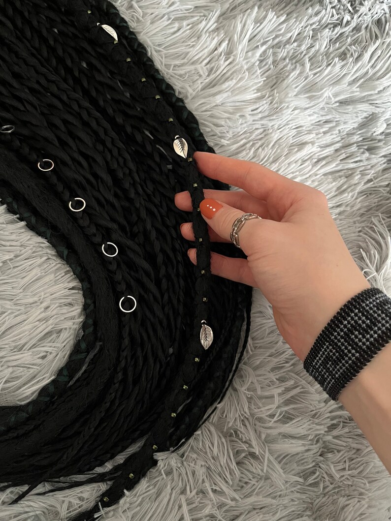 May include: Black synthetic hair extensions with small silver rings and leaf-shaped charms. The hair is braided and has a textured look.