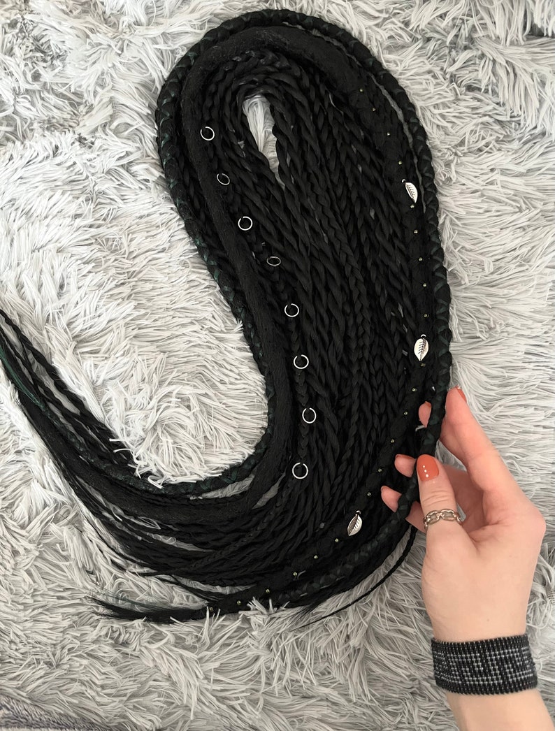 May include: A set of black synthetic hair extensions with silver beads and charms. The extensions are braided and arranged in a loose bundle.
