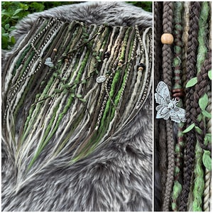 Puede incluir: Conjunto de rastas hechas a mano en tonos verdes, marrones y blancos, adornadas con cuentas de madera, dijes de mariposa de metal y vegetación artificial. Las rastas se presentan sobre una superficie de piel sintética gris, mostrando los detalles y la paleta de colores naturales.