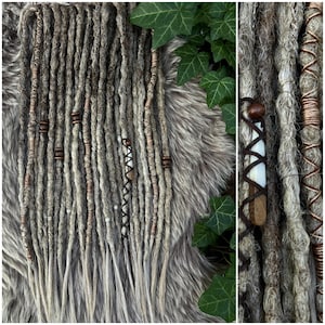 Könnte beinhalten: Nahaufnahme von grauen Dreadlocks mit braunen und silbernen Akzenten. Einige Dreadlocks sind mit braunem Faden umwickelt und mit Holzperlen verziert. Der Hintergrund ist eine pelzige, graue Oberfläche mit grünen Efeublättern.