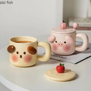May include: Two ceramic mugs with animal designs. One is light yellow with a dog face, the other is pink with a pig face. The pig mug has a lid with a peach-shaped handle. A small red apple decorates the lid of the other mug.