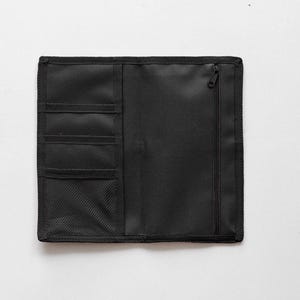May include: Black organizer with multiple pockets and a zippered compartment. The organizer has three small pockets, a mesh pocket, and a zippered section. The material appears to be a durable fabric.