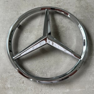Op de afbeelding: Een verchroomd Mercedes-Benz-logo met een driepuntige ster in het midden.