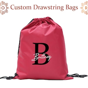 May include: A bright pink drawstring bag with a black letter "B" and the name "Brittney" in white lettering.