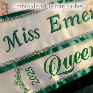 May include: White satin sashes with green embroidered text and accents. The sashes read "Miss Emerald" and "Queen 2025". Each sash has a green border and silver sequin trim. The top of the image reads "Embroidery Custom Sashes".
