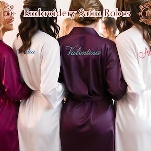 May include: Five satin robes in white and purple with embroidered names, "Ayra", "Nadia", "Valentina", "Ashley", and "Sarah". The robes are part of a bridal party set.
