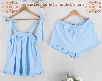May include: A blue and white striped seersucker ruffle camisole and shorts set. The camisole has thin straps and a ruffle trim. The shorts have a drawstring waist and a ruffle trim.