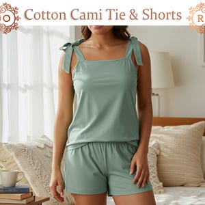 May include: A light green cotton cami top and shorts set. The cami has tie straps and a square neckline. The shorts are a matching color and have an elastic waistband. The text "Cotton Cami Tie & Shorts" is at the top of the image.