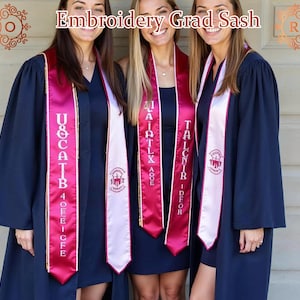 Può includere: Tre laureate indossano abiti blu navy e stole di laurea personalizzate. Le stole sono di un magenta intenso con scritte bianche e un stemma. Il testo "Embroidery Grad Sash" è nella parte superiore dell'immagine.