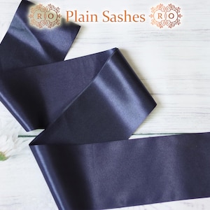 May include: A white ceramic mug with a black handle and the text "But First, Coffee" in a bold, black font. The mug is set against a blurred background, suggesting a cozy setting.