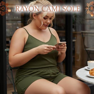 May include: Olive green rayon cami top and shorts set. The top has thin straps and a V-neck. The shorts have a matching color scheme. The text "RAYON CAMI SOLE" is displayed at the top of the image. The person is sitting at a table with a coffee and croissant.